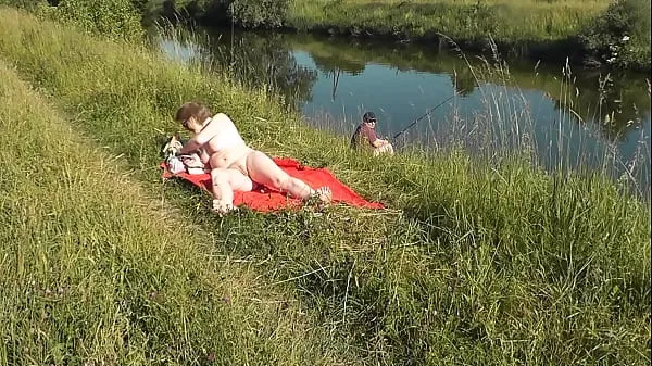 Veľká MILF sexy Frina on river bank undressed and sunbathes naked. Random man fisherman watching for her, and in the end decided to join naked woman. Wild beach. Nudist beach. Public nudity. Public exposure. Naked in public totálna trubica
